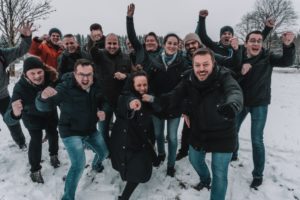 Weihnachtsfeier planen: Menschen stehen in einer Gruppe im Schnee und jubeln, weil sie eine schöne Wanderung im Rahmen ihrer Weihnachtsfeier machen.